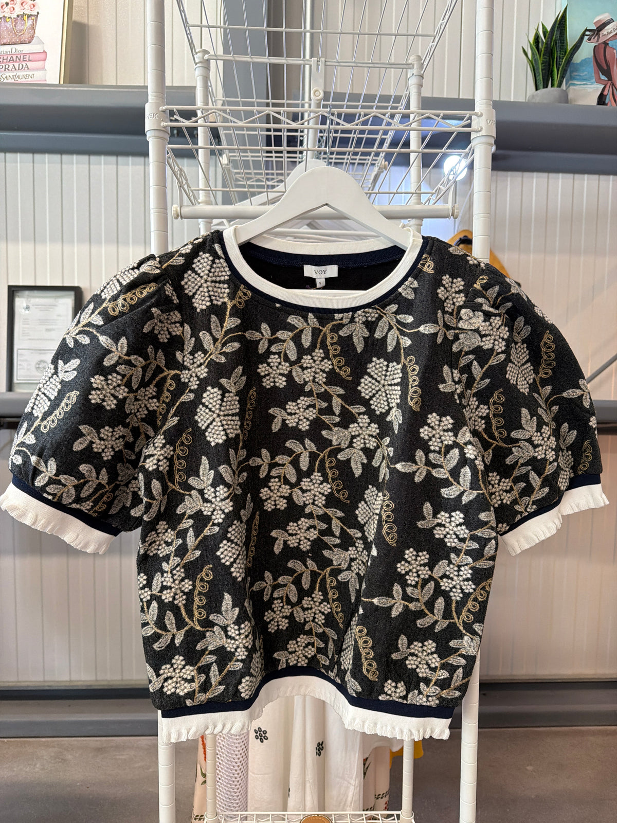 Elegant black knit sweater featuring a cream floral jacquard pattern with delicate gold embroidered accents. Puff short sleeves frame the shoulders beautifully, while cream contrast trim at the neckline and hem.