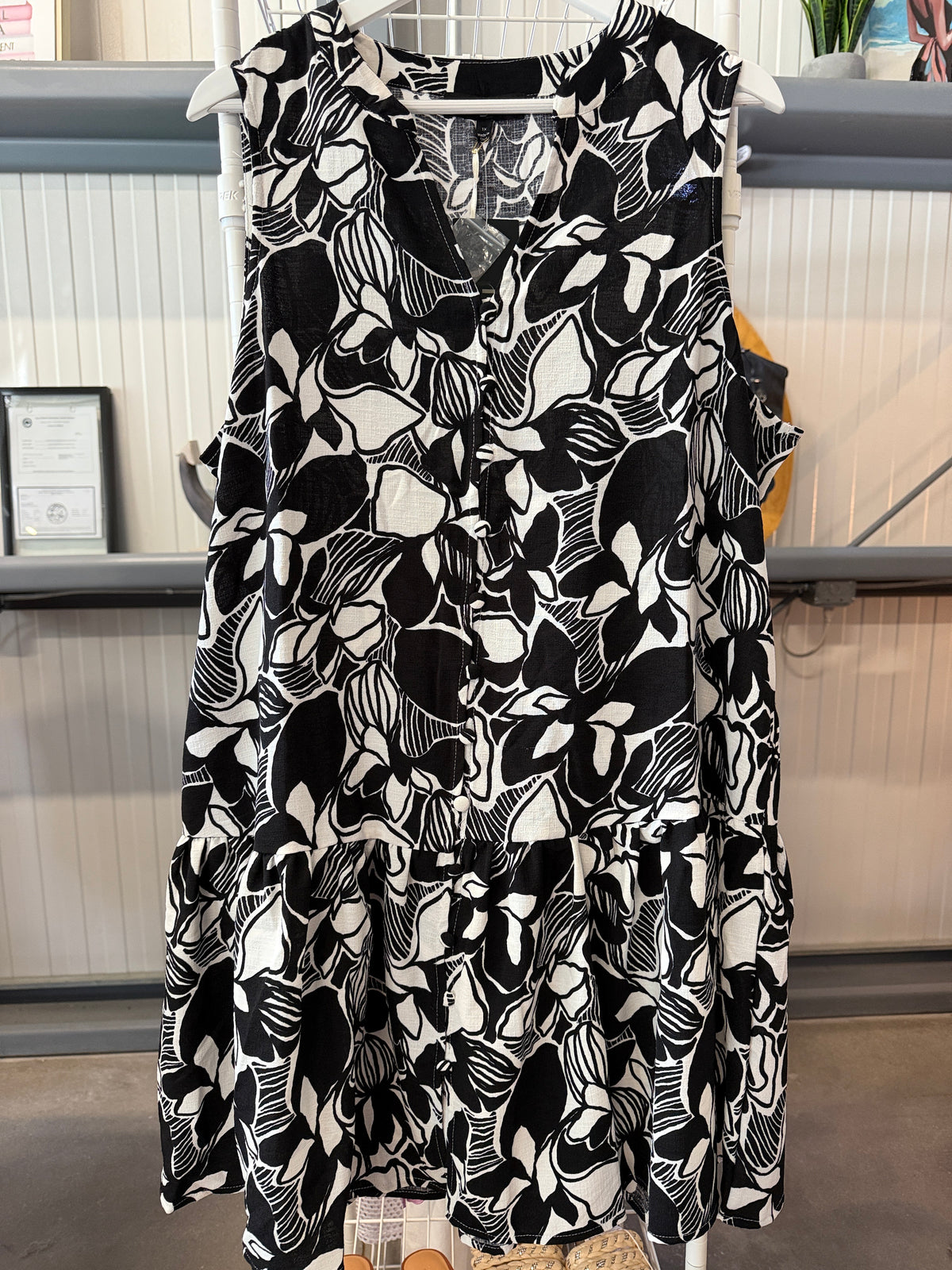 A sleeveless tiered mini dress with a bold black and white floral and leaf pattern, hanging on a white hanger in a retail store setting.