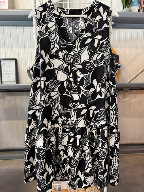 A sleeveless tiered mini dress with a bold black and white floral and leaf pattern, hanging on a white hanger in a retail store setting.